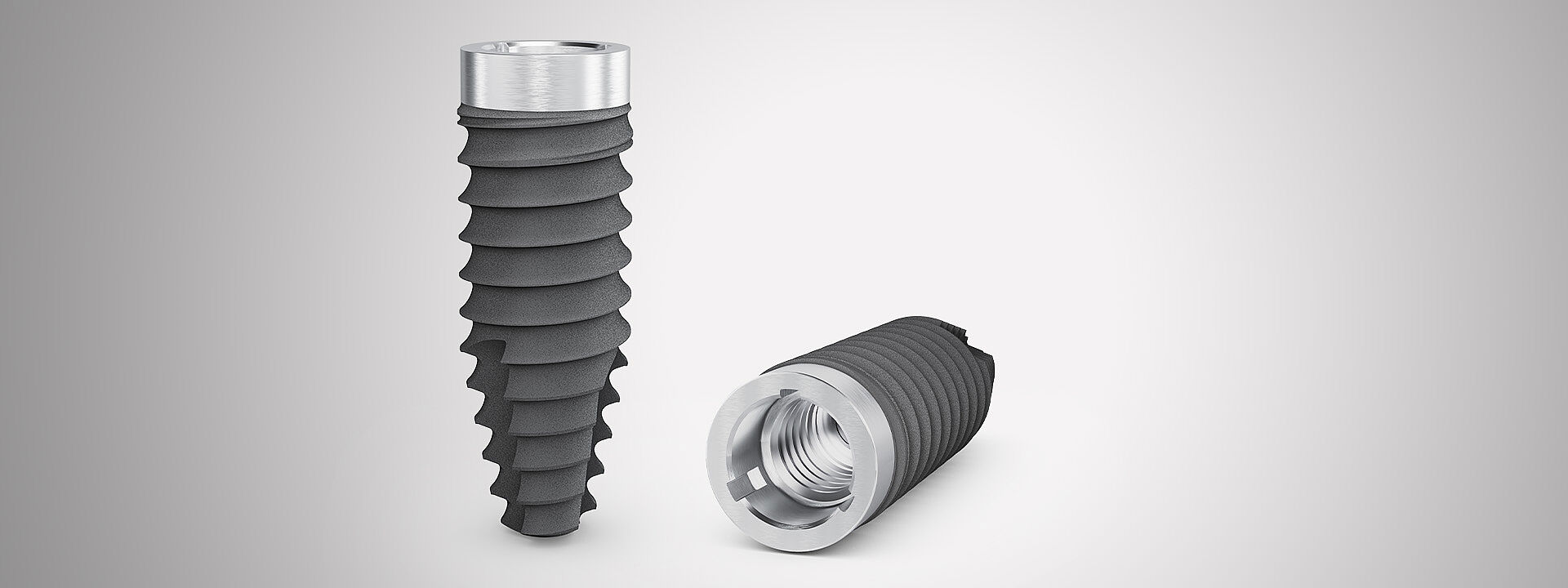 Zwei CAMLOG PROGRESSIVE-LINE Promote Implantate mit maschiniertem Implantathals von 1,4 mm Höhe vor breitem grau-weißem Hintergrund.